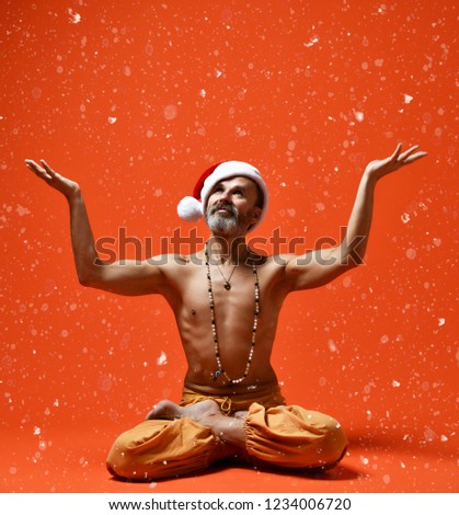 Sporty old man senior in red Santa Claus Christmas hat meditating in cross-legged yoga lotus pose, Padmasana, orange background