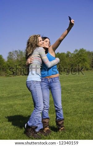 Beautiful Caucasian female teenages standing in a park and using a cell phone to take a picture.