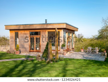 A wide view shot of a modern garden office on a bright summers day, a clear sky is above the wooden office and standing stones can be seen on the grass. Royalty-Free Stock Photo #1234026421