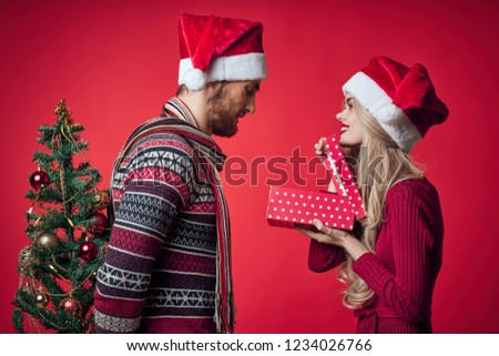 a woman with a gift box and a man with a dressed up Christmas tree in her hands behind her back                    