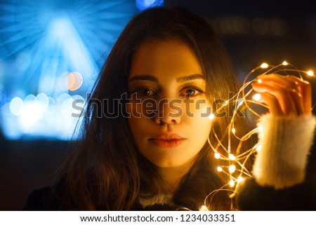 Portrait of a beautiful girl with luminous garland on the background of a ferris wheel in the night city.