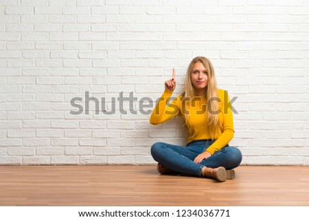 Young girl sitting on the floor showing and lifting a finger in sign of the best