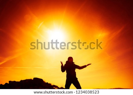 silhouette of man  against sunset sky with clouds above horizon. Man doing Yoga on peak of mountain at sun rays background. 