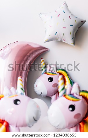 Adorable inflatable unicorn balloons with the pink mood and a star balloons on the grey wall background, vertical photo