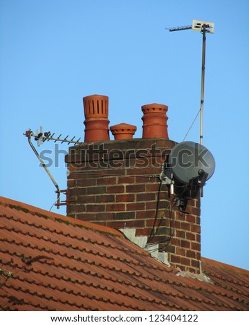 A typical chimney found on a domestic semi detached dwelling in the UK, with satellite dish and aerials,on a background of blue sky.