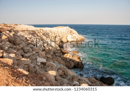 The rocky coast of Cyprus at sunset. Caves and cliffs of Greece. Waves at sea. Coral seacoast. 