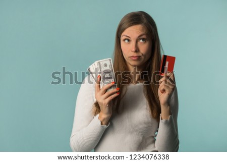 beautiful young girl holding dollars in her hands and a credit card on a blue background