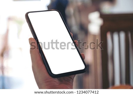 Mockup image of hand holding black mobile phone with blank white screen in vintage cafe