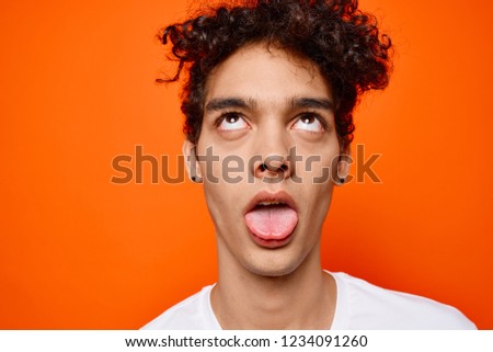 curly guy shows tongue on orange background                       