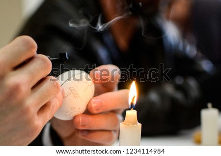 Closeup of hands holding candle and easter egg. Draw on an Easter egg.
