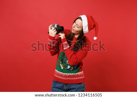 Curious young Santa girl in Christmas hat looking on retro vintage photo camera in hands isolated on bright red background. Happy New Year 2019 celebration holiday party concept. Mock up copy space