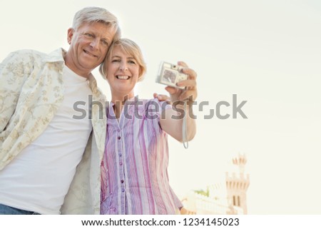 Beautiful senior couple visiting monument on vacation, sightseeing taking selfies with photo camera, smiling outdoors. Healthy mature people traveling, leisure recreation technology lifestyle.