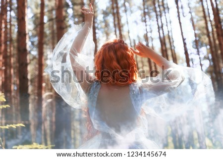 Beautiful redhead woman forest nymph in a blue transparent light dress in the woods spinning in dance. Red hair girls. Art fashion portrait of fairy woman fairy tale in summer forest