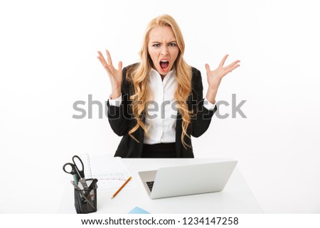 Photo of upset businesswoman sitting at table and working on laptop isolated over white background in studio