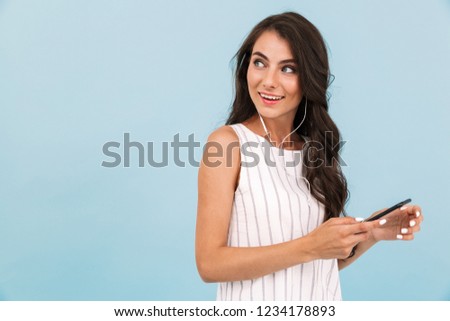 Image of beautiful young woman isolated over blue background wall listening music with earphones.
