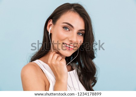 Image of beautiful young woman isolated over blue background wall listening music with earphones.