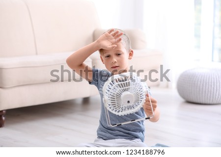 Little boy suffering from heat in front of fan at home Royalty-Free Stock Photo #1234188796