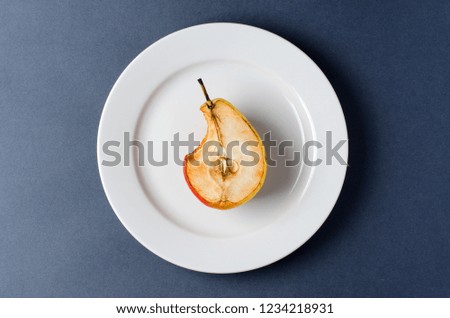 Stale old pear on a round white plate. Bite mark. Dark background
