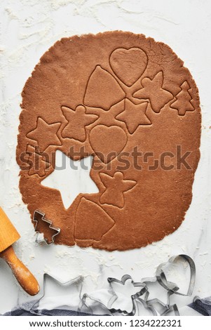 Gingerbread dough with various shape cookie cutout. Baking background for baking Christmas gingerbread cookies. Top view of cookie dough with cutters and rolling pin on white marble table.