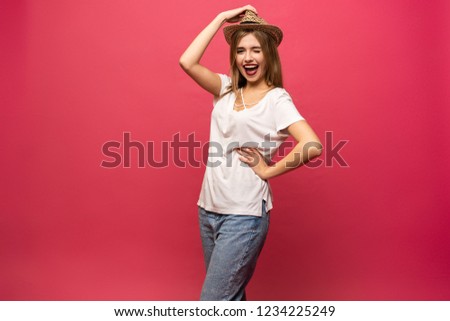 Studio portrait of cheerful female model holding summer hat and smiling. Blonde girl in sunglasses and white shirt having fun during photoshoot.