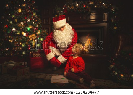 Real Santa Claus is playing with children near the Christmas tree. The atmosphere of celebration and magic.