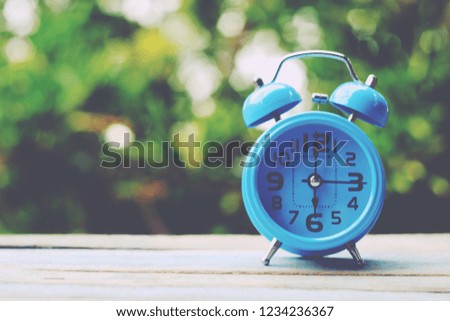 close up blue alarm clock on old wood table, green nature copy space background for text, saving and manage time to success business, countdown to holiday season, happy new year, vintage tone