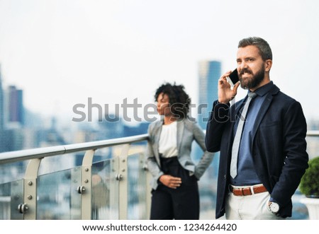 A portrait of a businessman with smartphone standing on a terrace.