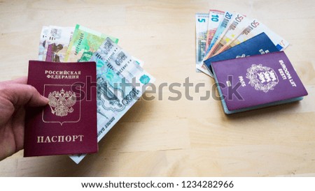 hand holding Passport on the wooden background with money. Citizenship of Estonia and Russia or European Union (EU) and Russian Federation. side view. Copy space design. Rubles and Euro banknotes. 