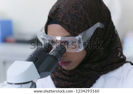 Young african muslim female scientist looking through a microscope in a laboratory doing research, microbiological analysis, medicine. Royalty-Free Stock Photo #1234293160