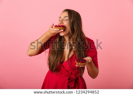 Image of a happy hungry young woman isolated over pink wall background holding cup cake.