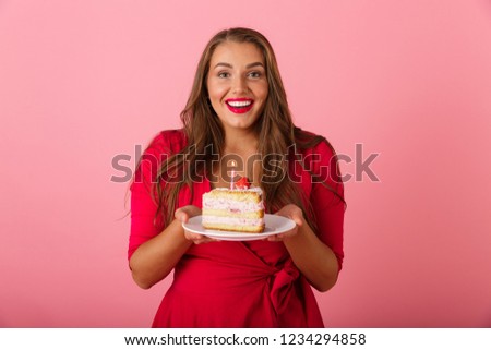 Image of an excited hungry young woman isolated over pink wall background holding cake.