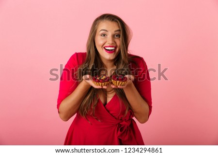 Image of a happy hungry young woman isolated over pink wall background holding cup cake.