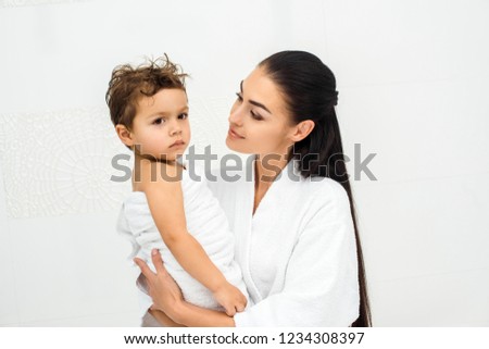 Mom holding and looking at son in towel on white