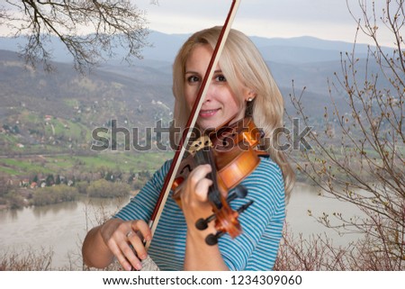 A beautiful blonde girl in blue dress plays a violin closeup Limited depth of field