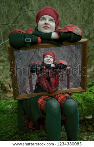 
a young girl in a red beret, a black coat and a skirt in a cage in the woods in autumn keeps her photo in a wooden frame. Concept psychology, narcissism