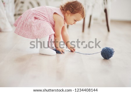 Childhood concept. Baby girl in cute dress play with colored thread. White vintage childroom.