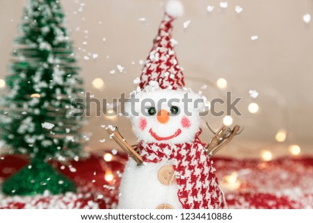 Snowman on snow over blurred christmas tree and light bokeh