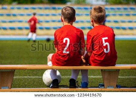 Kids Football Team. Two Young Boys Watching Soccer Match. Football Tournament Competition in the Background. Children Football Team Players in Red Jersey  Uniforms on The Soccer Stadium Royalty-Free Stock Photo #1234419670
