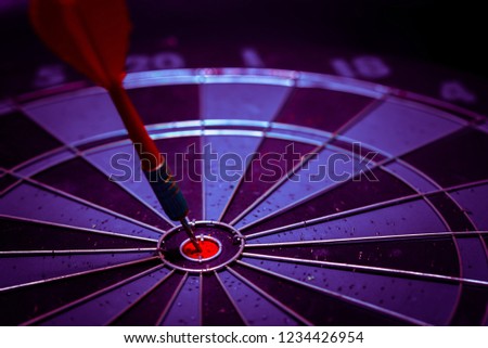 
Close up shot of the dart arrow hit on bulleyes of dartboard to represent that the business reached the target of company with dark tone picture style. Target and goal as concept.