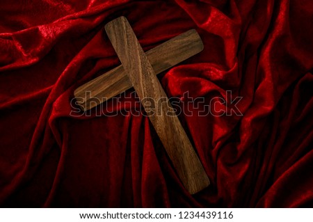 Christianity, easter holiday and religious faith concept with a backlit wood cross on red velvet with wave and wrinkles with dramatic moody light