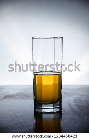 Natural drink of dark yellow color is typed in a glass on a lighted background.