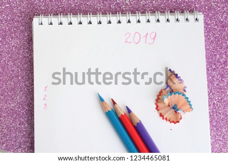 New year 2019 to do list in spiral white paper album. color pencils red violet and blue and notebook on shiny sparkle glittery pink background with selective focus. back to school.