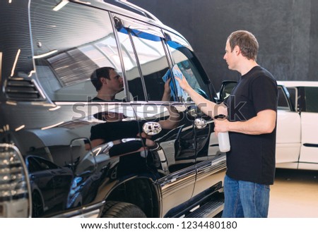 The man is wiping with a cloth body of a brilliant car.