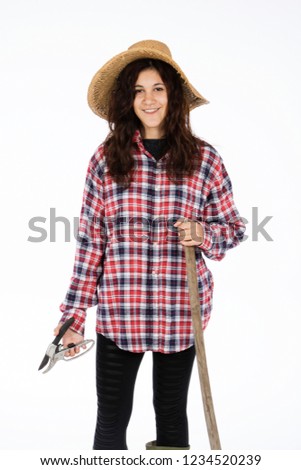 Young farmer with shears and hoe in hands, she is wearing a straw hat, checked shirt and green rubber boots