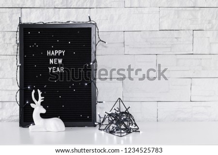 Happy new year text message on the dark board, figurine of a deer and black holidays decorations on the white background