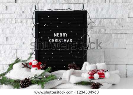 Merry Christmas phrase made with white letters on a black wooden desk with fir branches and winter decorations on white background