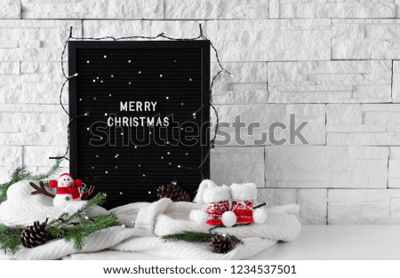 Merry Christmas phrase made with white letters on a black board with knitted sweaters and winter decorations on white background