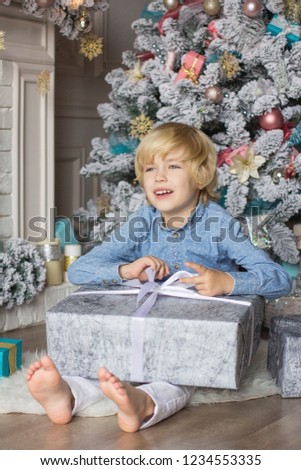 A handsome blond boy is sitting near the New Year tree