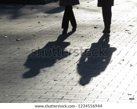 Silhouettes and shadows of two people walking down the street. Women outdoors, pedestrians on sidewalk, female friendship, concept for dramatic stories