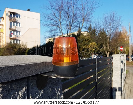 Orange room alarm light located on a brick fence post. Intercom apartment building at the entrance to a private protected area. Hazard alert. Intercom for door curtain. Property Protection and Securit